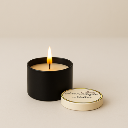 Classic Candle by Aromatique Atelier in black container with lid, lit and emitting warm glow, elegant minimalist design