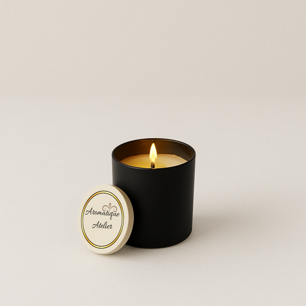 Premium Candle in black glass jar with lit wick and Aromatique Atelier bamboo lid placed beside it, eco-luxury soy-coconut wax blend scent